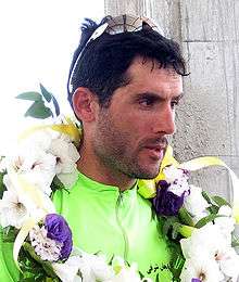 A man with parrot-green color athlete's attire, sunglasses on his head and a flower garland around his neck