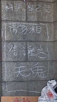 White Chinese characters chalked on a stone wall. Two at the bottom are larger than the others