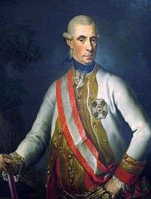 Painting of a long-faced man with heavy eyebrows who wears a white wig with large curls over the ears. He wears a white military coat with gold braid on the lapels and a red and white sash over his right shoulder.