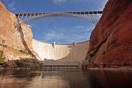 The Glen Canyon Dam and bridge, seen from the calm surface of the river at its base.