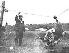 A man pulling a wire above his head, and another smaller man crashing into what hangs from the wire