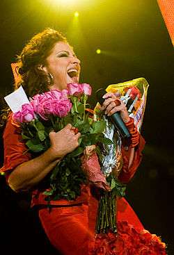 Gloria Estefan onstage, singing and holding flowers