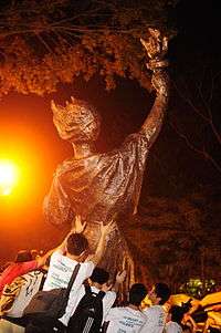 some people pushing a large bronze statue into an upright position by streetlight