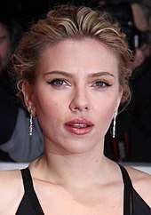An image of Scarlett Johansson posing for the camera with paparazzi in the background.