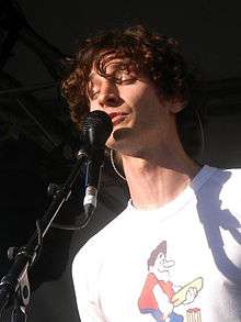 A Caucasian man with curly hair sings into a microphone.
