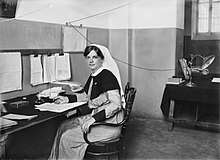 Black and white portrait photograph of a young woman wearing a nurses uniform while seated at a desk