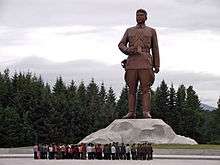 A crowd looking at a large statue depicting young Kim Il-sung in military attire