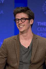 Grant Gustin, smiling and wearing morn-rimmed glasses