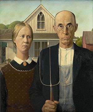 Man and woman with stern expession stand side-by-side. The man holds a pitch fork and wears glasses.