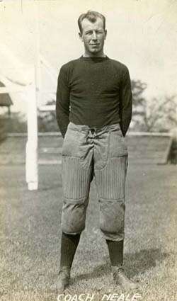 A man wearing an old-style football sweater and pants with high socks standing on a grass field with his hands behind his back
