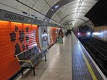 An underground station platform with curving red tiled walls and a white panelled ceiling arching over the track