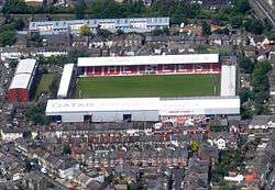 A white roofed football stadium with red seats seen from the air. It is surrounded by residential housing