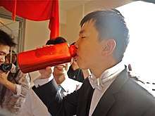 A groom drinking from a translucent red water bottle.