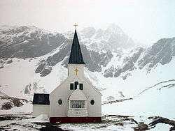 A white wooden church nestled within snow-covered mountains.