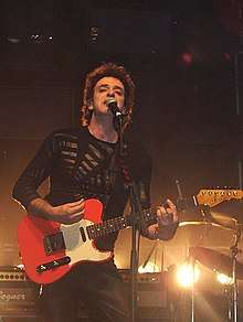 A man with a black shirt playing the guitar.