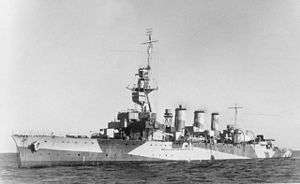 Black and white photograph of a World War II-era warship. The ship is painted in a camouflage pattern.