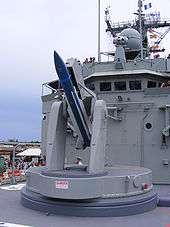 Close up of a naval missile launcher. A blue missile with white fins has been loaded.