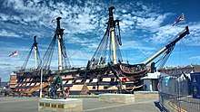 A picture of HMS Victory, the world's oldest commissioned naval ship, situated in Portsmouth's dry dock. The ship itself is missing its figurehead in this photo but retains its original sails.