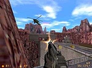 A video game screenshot depicting a gun being fired at a helicopter from a first-person perspective. The person from which the perspective of the image is taken is standing near a dam in a mountainous area, albeit with no visible water.