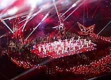 A faraway image of a stage with a performance going on, surrounded by a huge crowd.