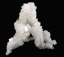 White crystals form a mineral sample of halite, shown against a black background.