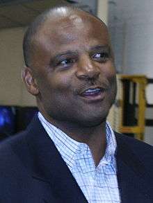 Color head-and-shoulders photograph of African-American man (Warren Moon) wearing a navy blazer and open-collar white tattersall shirt.