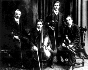 four musicians with string instruments in a posed group photograph