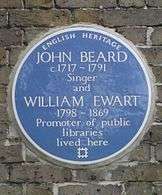 A Blue plaque on a brick wall with the words "John Beard C1717&nbsp;– 1791 Singer and William Ewart 1798&nbsp;– 1861 Promoter of Public Libraries