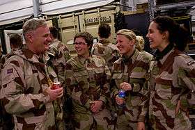 One man and three women in military fatigues converse while standing