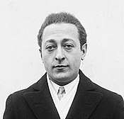 head and shoulders shot of a man in overcoat, jacket and tie, looking at the camera