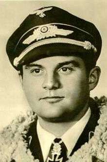 The head and shoulders of a young military man, shown in semi-profile. He wears a peaked cap and a pilot's leather jacket with a fur collar, with an Iron Cross, identifying him as a Nazi, displayed at the front of his shirt collar.