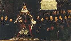 King Henry&nbsp;VIII in full royal regalia surrounded by a kneeling group of men who are all wearing black clothing and some with matching close-fitting caps