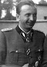 A black-and-white photograph of a smiling man in semi profile wearing a military uniform and a neck order in shape of an Iron Cross.