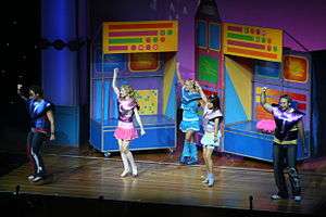 A stage shot of five performers in bright clothes, dancing.