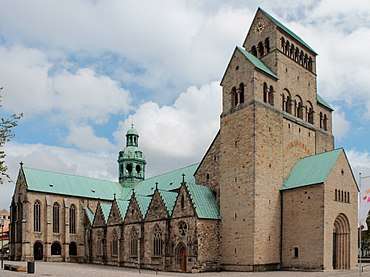 A romanesque stone cathedral, view of the north side. The green copper dome over the transept crossing is visible.
