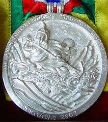 A silver medallion with an embossed image of Guru Rinpoche using a hand-drawing plow to harrow the sacred Rolwaling Valley. Around the upper edge is the text "Sir Edmund Hillary Mountain Legacy Medal"; at bottom is the text "Namche 2003"