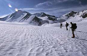 Three mountaineers on a snow-covered icefield with mountain peaks in the distance