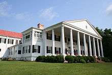 A two-story white house with red roof and columned porch.