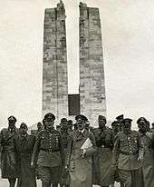 A group of men dressed in Nazi German soldier, front and centre is Adolf Hitler, June 1940. The twin pylons of the memorial are clearly displayed in the background.