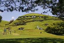 Image shows rolling green hills with dwellings built in to them. These formed the town of "Hobbiton" in the Lord of the Rings films. These and other sets were constructed near the town of Matamata, in the Waikato region of New Zealand's North Island.