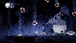 Gameplay screenshot of Hollow Knight, in which the player is fights a large boss enemy
