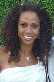 A woman with shoulder-length brown hair, wearing a white dress and a necklace