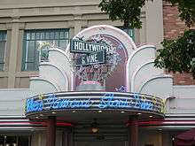 A photograph of a marquee reading "Where Famous Stars Dine" in blue over a doorway labelled 424 all under mock street signs, one reading "HOLLYWOOD" and the other reading "& VINE"