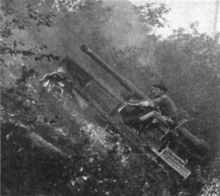 A tracked vehicle fitted with a large gun negotiates its way up a steep hillside (about 45˚, or one-in-one). The crew of two in the open cab are leaning forward and holding on tightly to avoid falling out backwards.