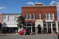 Photo of a two-story brick and stone building in a downtown area, a car parked in front.