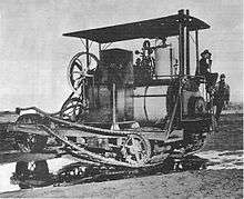 A machine similar in arrangement to the Holt seventy-five tractor, but with a steam boiler where later models would have the internal combustion engine fitted. A prominent chain drive extends the length of the vehicle from the steam engine to the rear, tracked wheels.