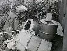 Pictured are home-made explosives packed in oil drums after having been dragged out of a culvert under a road. A soldier in a bomb suit kneels next to them.