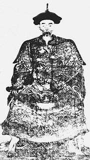 A full face black-and-white portrait of a sitting man with a gaunt face, wearing a robe covered with intricate cloud and dragon patterns.