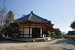 A small wooden octagonal building with white walls on a stone platform.