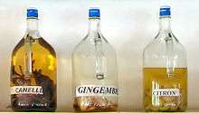 three bottles of liquid in various colors on a shelf, labeled "cinnamon," "ginger" and "lemon"